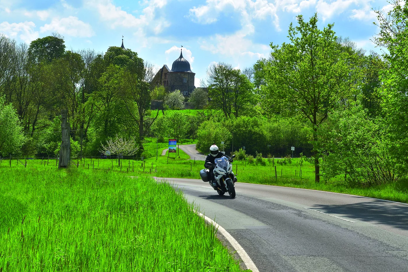 Motorrad auf der Landstraße, dahinter die Türme der Sababurg über den Wiesen Motorrad auf der Landstraße, dahinter die Türme der Sababurg über den Wiesen